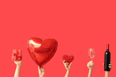 Kalp şeklinde balonu, bardağı, şarap şişesi ve kırmızı arka planda hediye kutusu olan kadın elleri. Sevgililer Günü kutlaması