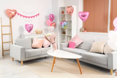 İçinde gri koltuklar, kalp şeklinde balonlar ve sehpanın üzerinde güller olan şenlikli oturma odasının içi. Sevgililer Günü kutlaması