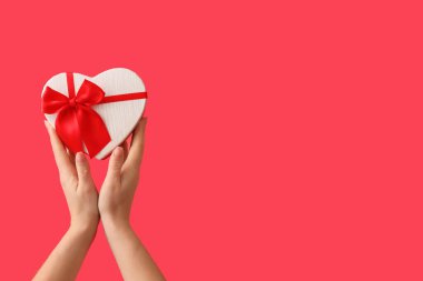 Kırmızı arka planda kalp şeklinde hediye kutusu tutan kadın elleri. Sevgililer Günü kutlaması
