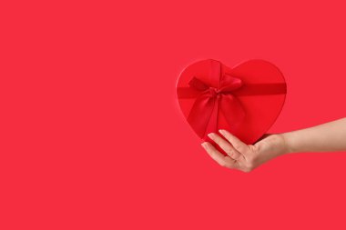 Kırmızı arka planda kalp şeklinde hediye kutusu tutan bir kadın. Sevgililer Günü kutlaması