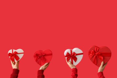 Kırmızı arka planda kalp şeklinde hediye kutularını tutan kadın elleri. Sevgililer Günü kutlaması