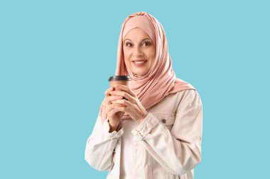 Mavi arka planda bir fincan kahveyle tesettürlü olgun Müslüman kadın