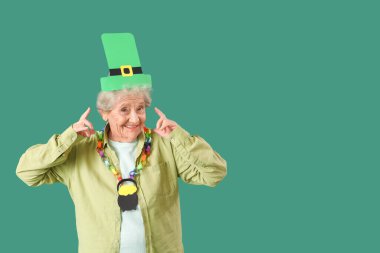 Yeşil arka planda Aziz Patrick Günü kutlamaları için kağıt leprikon şapkayı gösteren mutlu yaşlı kadın.