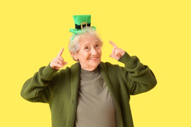 Sarı arka plandaki cüce şapkayı gösteren mutlu yaşlı kadın. Aziz Patrick Günü kutlaması