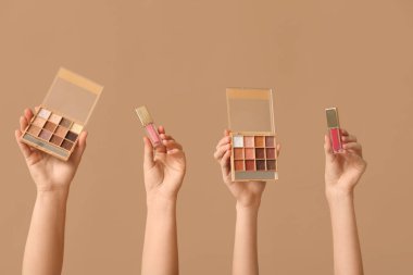 Göz farı paletleri ve bej arka planda dudak parlatıcısı olan kadın elleri