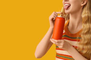 Sarı arka planda soda kutusu olan genç bir kadın.