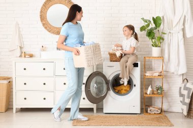 Genç bir kadın ve kızı çamaşır makinesinden çamaşır çıkartıyorlar.