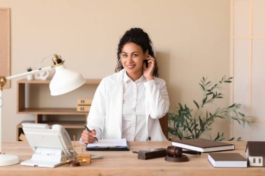 Female African-American lawyer working at table in office clipart