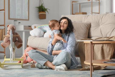 Güzel, genç, mutlu bir anne. Evinde farklı oyuncaklarla küçük bebeğine sarılıyor.