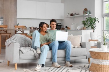 Genç çift evdeki kanepede dizüstü bilgisayar kullanıyor.