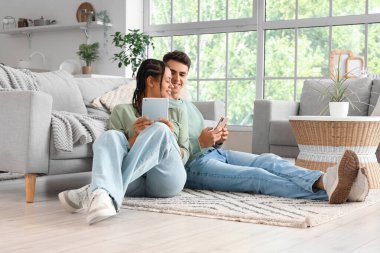 Evde tablet bilgisayar ve cep telefonu kullanan genç bir çift.