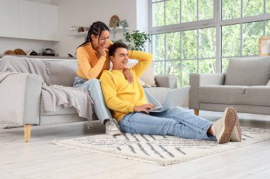 Evde dizüstü bilgisayardan film izleyen gülen genç çift.