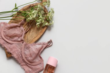 Şık dantel sutyenli kompozisyon, bir şişe parfüm ve gri arka planda çiçekler