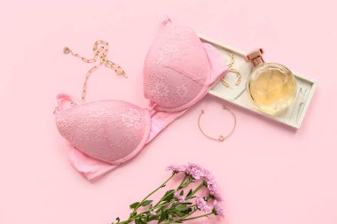 Sütyenli kompozisyon, bir şişe parfüm ve pembe arka planda aksesuarlar.