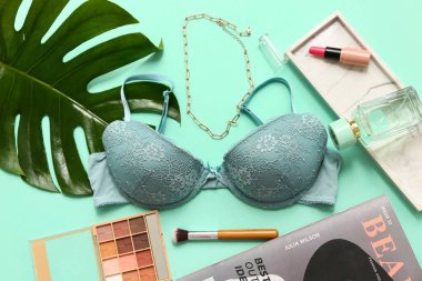 Renkli arka planda şık kadın sütyeni, kozmetik, aksesuar ve palmiye yaprağı kompozisyonu