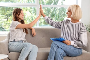 Genç kızla birlikte kadın psikolog ofiste beşlik çakıyor.