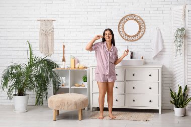 Banyoda dişlerini fırçalayan genç bir kadın.