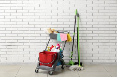 Beyaz tuğla duvarın yanında temizlik malzemeleri olan bir tramvay.