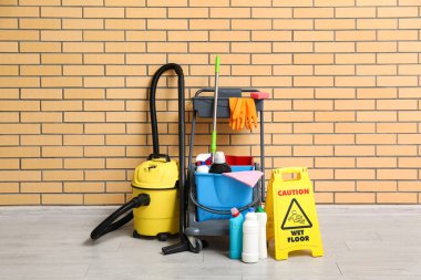 Temizlik malzemeleri, uyarı levhası ve tuğla duvarın yanındaki elektrikli süpürge.