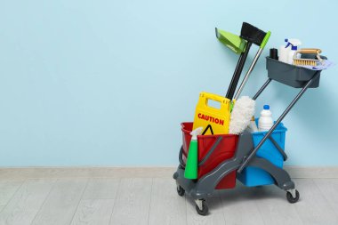 Temizlik malzemeleri ve mavi duvarın yanında uyarı levhası olan kapıcı vagonu.