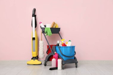 Temizlik malzemeleri ve elektrikli süpürgeyle birlikte pembe duvarın yanında kapıcı vagonu.