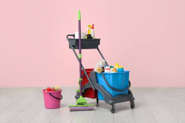 Temizlik malzemeleri ve pembe duvarın yanında yer paspası olan kapıcı vagonu.