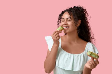 Afro-Amerikalı bir kadın pembe arka planda lezzetli ekinler yiyor.