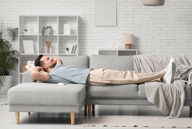 Oturma odasındaki klimalı kanepede dinlenen yakışıklı genç adam.