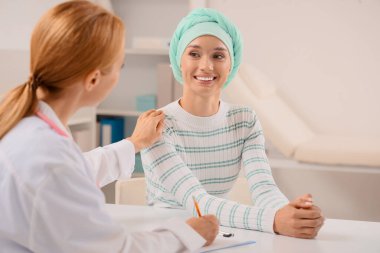 Kemoterapiden sonra klinikte doktorla gülümseyen genç bir kadın.