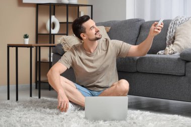 Evde dizüstü bilgisayar kullanırken klimayı açan yakışıklı genç adam.