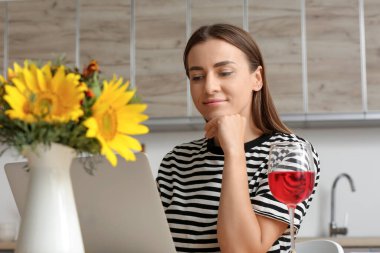 Mutfaktaki masada dizüstü bilgisayar kullanan genç bir kadın.