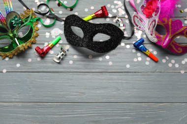 Gri ahşap arka planda parti boynuzları ve konfetileri olan güzel karnaval maskeleri. Üst görünüm