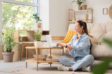 Evdeki sehpada dizüstü bilgisayar kullanan genç bir kadın.