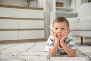 Evdeki halıya uzanmış düşünceli küçük çocuk.