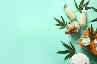 Turkuaz arka planda kenevir kozmetik yağı, deniz tuzu, yaprak ve krema kavanozları
