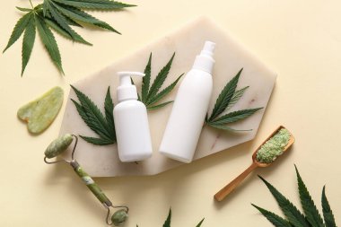 Deniz tuzu, yüz masajı aletleri ve bej arka planda yapraklarla kenevir kozmetik ürünleri.