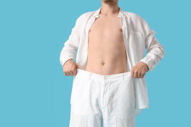 Mavi arka planda bol pantolonlu genç adam. Kilo verme konsepti