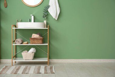 Modern lavabo, raf ünitesi ve banyo malzemeleri banyoda yeşil duvarın yanında.