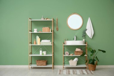 Modern lavabo, raf üniteleri ve banyo malzemeleri banyonun içindeki yeşil duvarın yanında.