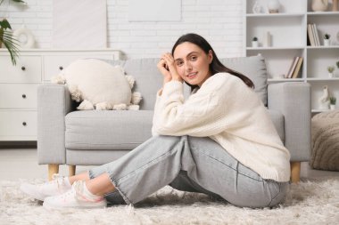 Evdeki halıda dizüstü bilgisayarı olan genç bir kadın.