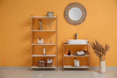 Beyaz seramik lavabo ve banyoda banyo aksesuarları olan raf ünitesi.