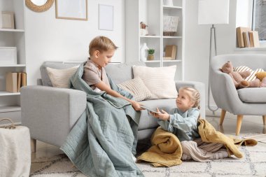 Ekose kumaşlı küçük çocuk evde kız kardeşine tablet veriyor.