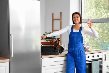 Mutfaktaki buzdolabının yanında bir çanta alet edevat taşıyan kadın işçi.