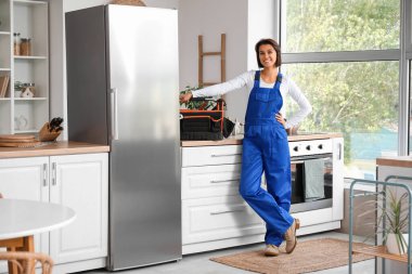 Mutfaktaki buzdolabının yanında bir çanta alet edevat taşıyan kadın işçi.