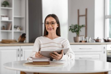 Mutfaktaki masada kitap okuyan genç ve güzel bir kadın.