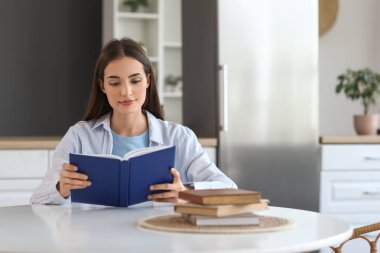 Mutfaktaki masada kitap okuyan güzel genç bir kadın.
