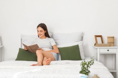 Güzel, genç, mutlu bir kadın evde kitap okuyor.