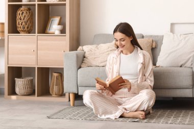 Pijamalı güzel, genç bir kadın evde kitap okuyor.