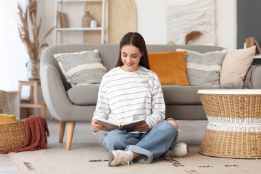 Güzel, genç, mutlu bir kadın evde kitap okuyor.