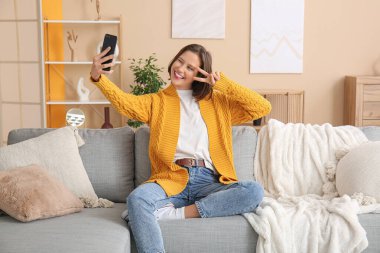 Cep telefonlu güzel bir kadın evdeki kanepede selfie çekiyor.